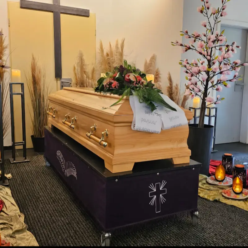Hellbrauner Sarg mit Blumen und Kerzen vor Kreuz und Kirschbluetenbaum