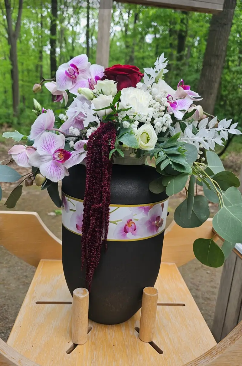 Elegantes Bouquet mit Orchideen und roter Rose in schwarzer Vase im Wald